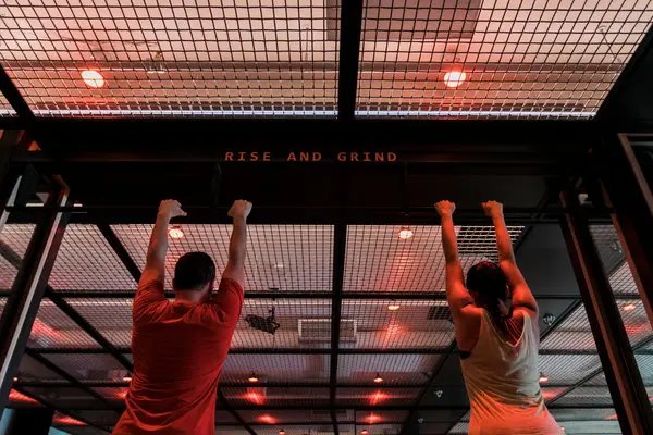 Members training on the overhead rig beneath a Rise and Grind sign
