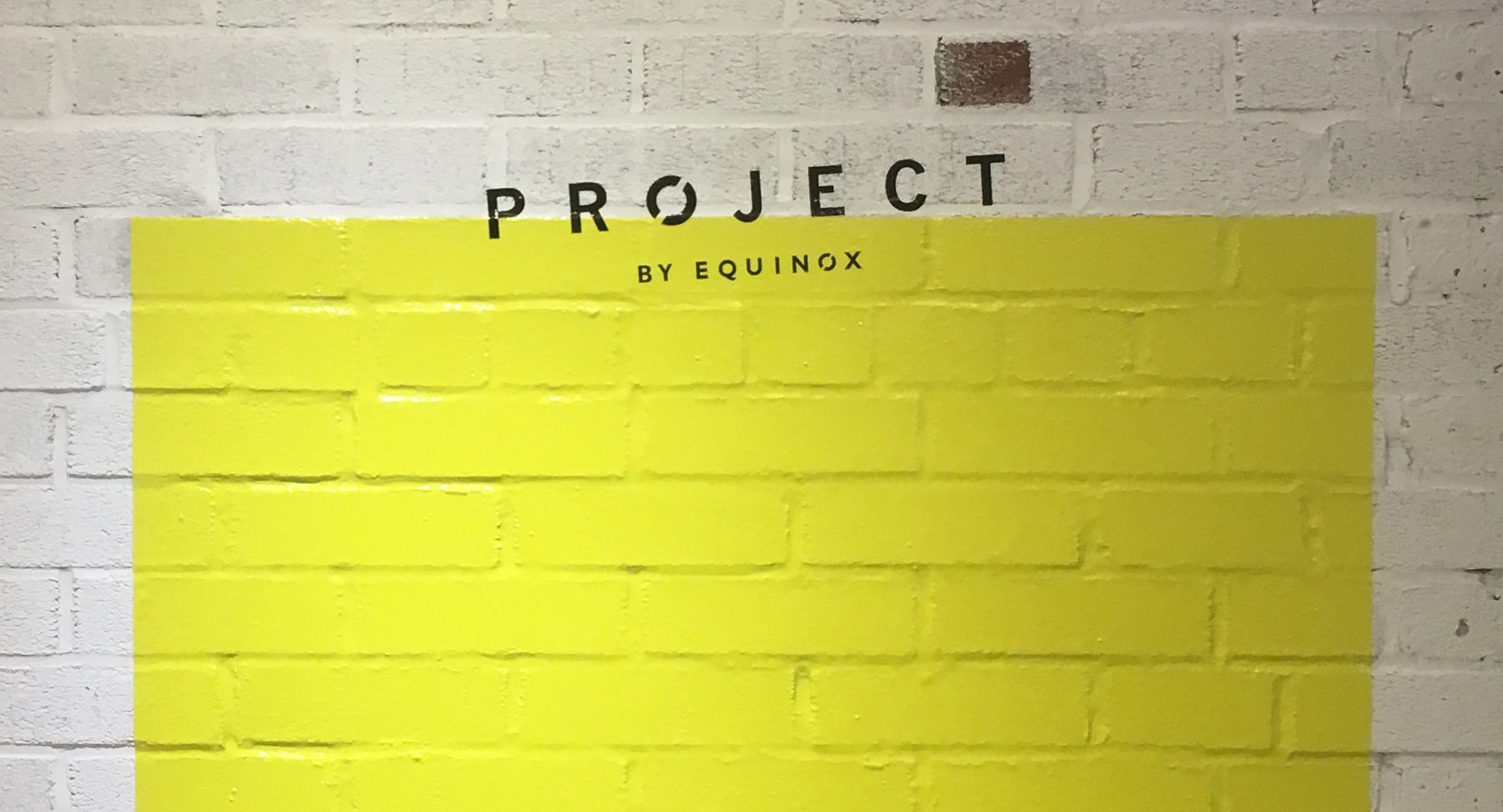 PROJECT graphic in yellow on a white brick wall