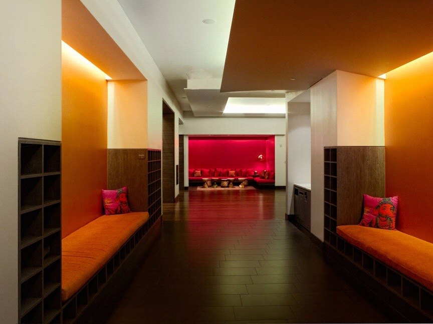 Corridor with orange banquettes opening to a red-lit lounge
